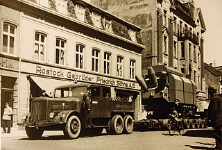 Der Culemeyer im Einsatz: Hier zieht er ein Riesenaggregat der AEG vom Güterbahnhof durch die Schulstraße zum Kunden. Im Hintergrund die Marinefrabrik Rostock, die später C&A wich. Heute steht dort ein Wohnblock inklusive Postbank. (Foto: Per Koopmann / Stadtarchiv)  